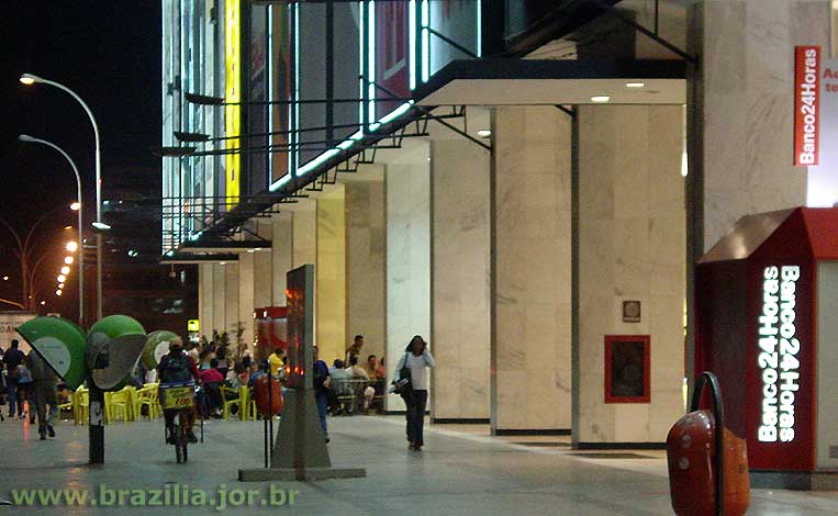 Fachada de anúncios luminosos, amplas entradas de pé direito duplo e mesas na calçada são características do Conjunto Nacional planejadas por Lúcio Costa no projeto de Brasília